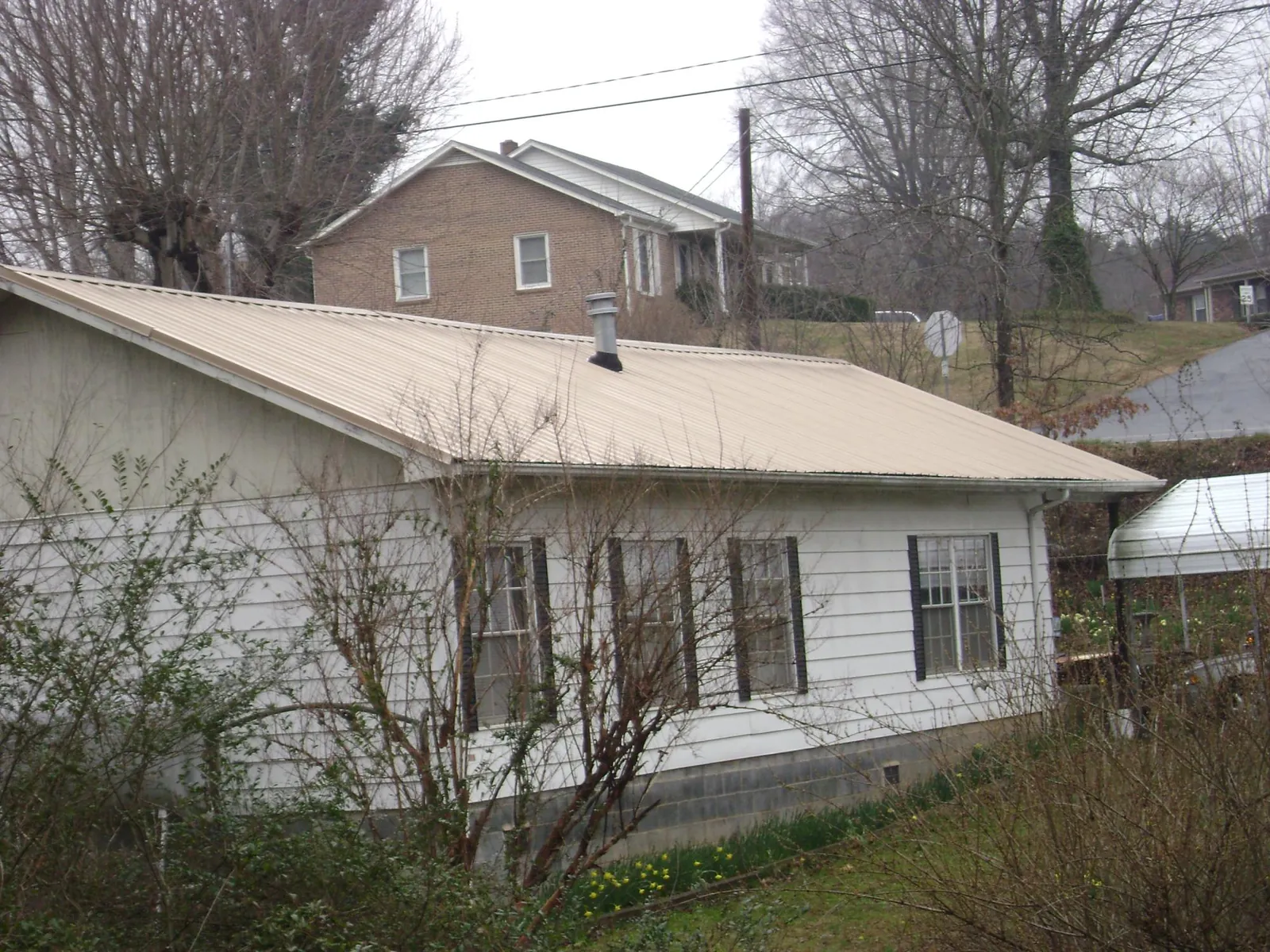 Tan metal roof on a white sided house set into a hillside — Commercial Roofing by Roofing Brothers in Palmyra